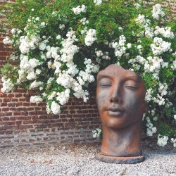 statue visage femme en pierre mur fleurs